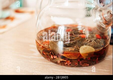 Reste von gebrühtem grünen heißen Tee mit Himbeeren und Beeren in einer schönen Glaskanne auf einem Holztisch. Natürliches Licht, Lifestyle, Stimmungsfarbe Stockfoto