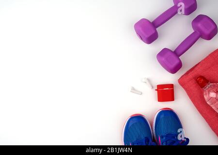 Violette Kunststoff-Hanteln, Wasserflasche, blaue Sneaker und drahtlose Kopfhörer auf weißem Hintergrund, Fitness-Kit, flaches Lay, Kopierraum Stockfoto