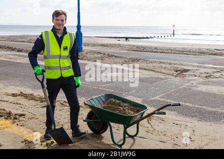 Bournemouth, Dorset, Großbritannien. Februar 2020. Stadtrat Lewis Allison bleibt stecken und gibt den Rangern am Meer eine Hand, um den Sand von der Promenade zu entfernen, der von den jüngsten starken Winden und dem Sturm Dennis geblasen wurde. Stadtrat Allison ist Labour-Ratsherr für Boscombe West und Portfolio-Inhaber, Kabinettsmitglied, für Tourismus, Freizeit und Gemeinden im BCP-Rat (Bournemouth, Christchurch und Poole). Credit: Carolyn Jenkins/Alamy Live News Stockfoto