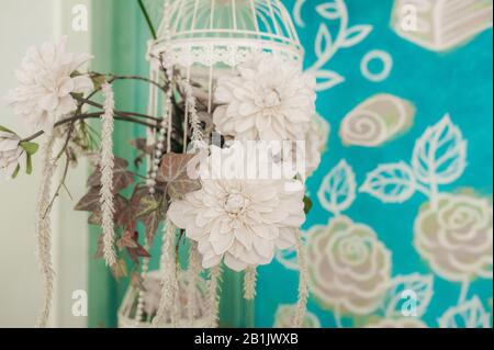 Wanddekor im Zimmer, weiße künstliche Blumen in einer hängenden Vase auf einem Hintergrund aus bemalter blauer Blume. Stockfoto