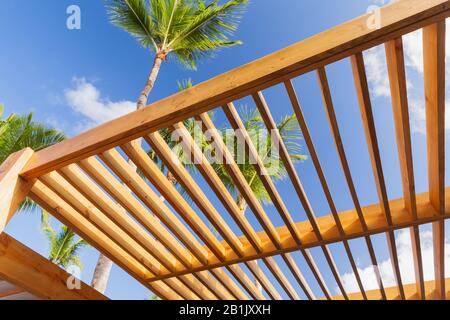Holz-Sonnenschutz-Dachbaufragment unter blauem Himmel am sonnigen Sommertag stehen Palmen auf dem Hintergrund Stockfoto