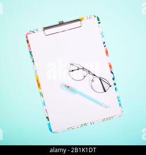 Leeres Papier auf farbiger Zwischenablage mit Kopierbereich auf hellem Neo-Mint-Hintergrund mit Brille. Draufsicht, flacher Lay. Stockfoto