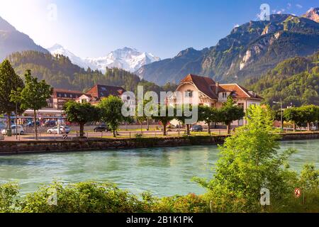 Bahnhof und Fluss Aare in Interlaken, wichtiges Touristenzentrum im Berner Hochland, Schweiz. Die Jungfrau ist im Hintergrund zu sehen Stockfoto