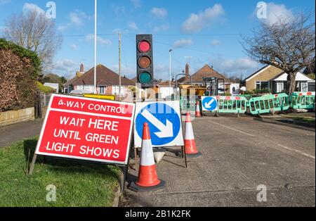 "Warten Sie hier, bis grünes Licht aufleuchtet" Warnschild an einer 4-Wege-Kreuzung an Straßenbaustellen, mit vorübergehender Ampel in England, Großbritannien. Stockfoto