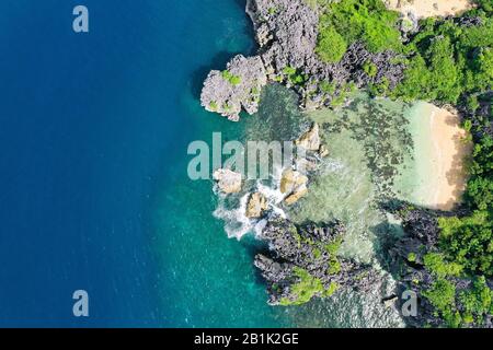 Matukad Island, Karamoische Inseln, Philippinen. Wilder weißer Sandstrand. Sommer- und Reiseurlaubskonzept. Felseninsel mit weißem Sandstrand, Blick von oben. Luftaufnahme von oben auf Wellen, Strand und felsige Küste und wunderschönen Wald. Stockfoto