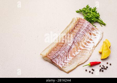 Rohpollockfilet (Pollachius virens). Frischer Fisch für gesunden Lebensstil. Zitrone, Petersilie, Meersalz, Chili, schwarzes Pfeffermais. Steinbeton Backg Stockfoto