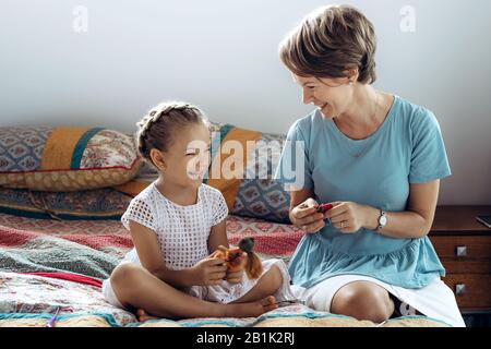 Mutter und ihre kleine Tochter reden und lachen auf dem Bett. Stockfoto