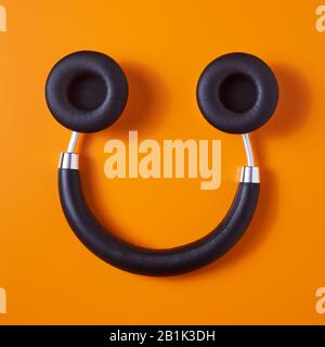 Ein Paar schwarzer drahtloser Kopfhörer mit voller Größe, oben auf orangefarbenem Hintergrund, der einem Smiley-Gesicht ähnelt, ist in einem hohen Winkel zu sehen Stockfoto