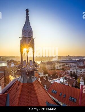 Budapest, Ungarn - Alter traditioneller Metallturm und rote Dächer des Burgviertels mit aufsteigender Sonne, St. Stephens-Basilika und Szechenyi-Kettenbrücke Stockfoto