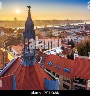 Budapest, Ungarn - Alter traditioneller Metallturm und rote Dächer des Burgviertels mit aufsteigender Sonne, St. Stephens-Basilika und Szechenyi-Kettenbrücke Stockfoto