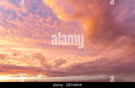 Rosafarbener Himmel mit verstreuten Wolken während eines orangefarbenen Sonnenuntergangs Stockfoto