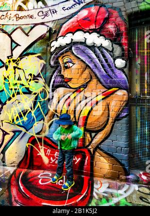 Großes Graffiti-Gemälde im Cartoon-Stil einer Frau mit Weihnachtshut und jungen Jungen, die auf der Straße stehen, Hosier Street, Melbourne Lanes, Melbourne, Vic Stockfoto