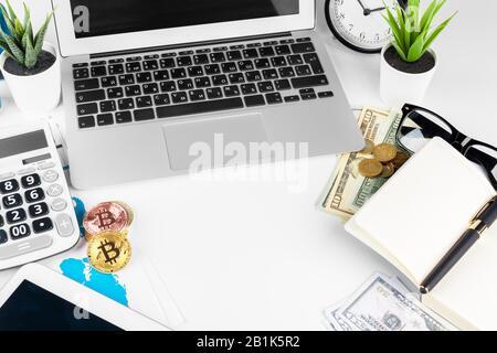Laptop auf dem Tisch in der Nähe von Dollars und Bitcoins im Büro. Kreatives Foto. Stockfoto