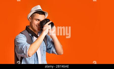Aktiver glücklicher Reisender, der Fotos mit der Kamera über orangefarbenem Hintergrund macht Stockfoto