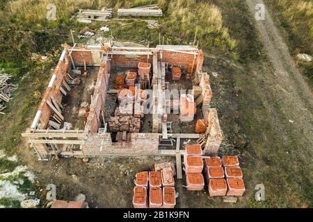 Luftbild der Baustelle für zukünftiges Ziegelhaus, Betonfundament und Stapel gelber Lehmziegel für den Bau. Stockfoto