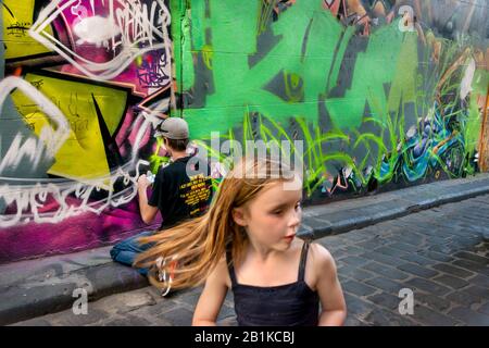 Der junge Mann, der das Design des Handykopierens betrachtet, um Graffiti an die Wand zu sprühen, wobei das junge Mädchen den gepflasterten Gasse aus Stein, Hosier Stre, aufläuft Stockfoto