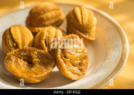 Kleine Plätzchen in Form von Walnüssen auf einer weißen Untertasse. Süßigkeiten auf dem sonnigen Tisch. Stockfoto