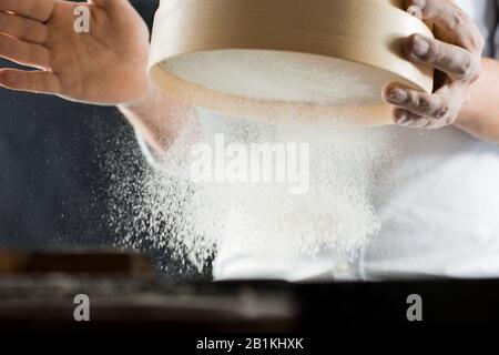 Männliche Hände eines Kochs sieden Mehl durch ein Sieb in der Seitenansicht der Küche Stockfoto