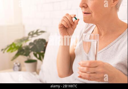 Gesunde Seniorin, die Pillen mit Glas Wasser im Bett nimmt Stockfoto