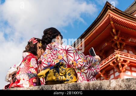 Junge Frauen, die Selfies nehmen, gekleidet in Kimonos, das für den Tag gemietet werden kann, außerhalb von Kiyomizu-dera, einem unabhängigen buddhistischen Tempel im Osten Kyotos