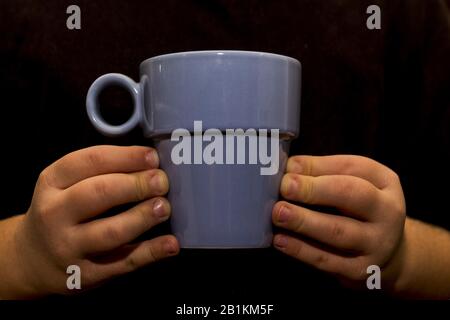 Die Hände des Kindes halten eine Tasse Stockfoto