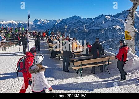 Osterfelderkopf - das Restaurant Alpspitz ist mit 2.033 m das höchste Restaurant im klassischen Ski- und Wandergebiet von Garmisch-Partenkirchen. Es befindet sich in der Bergstation der Alpspitzbahn, wo Sonnenanbeter, Exkursionisten und Skitouristen auf Bänken sitzen und die großartige Aussicht sowie wunderbares Wetter, Sonnenschein und Sonne genießen. Skifahrer in den bayerischen Alpen, Skigebiet Garmisch Classic, Bayern, Deutschland, Skifahren, Fahren, Skifahren, Skiurlaub, Sonnenschein, Blick, Freizeit, Sport, Landschaft, Aktivität, Schnee, Wintersport, Wintersportler, Wintersportgebiet, Berge, Schnee, Stockfoto