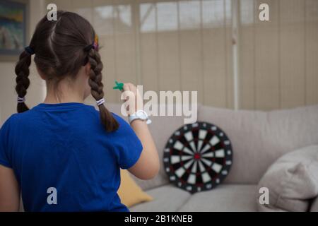 Ein junges Mädchen, das zuhause Darts spielt Stockfoto