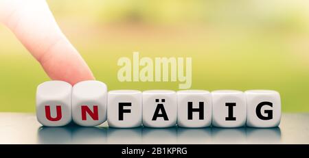 Hand dreht Würfel und ändert das deutsche Wort "unfaehig" ("inkompetent") in "faehig" ("kompetent"). Stockfoto