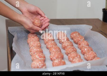 Weibliche Hände machen im Backofen Fleischbällchen. Schwedisches Rohmekatkugeln. Hausgemachte gebratene Rinderpatten. Auf Pergament gebacken Stockfoto