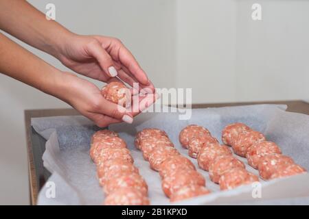 Weibliche Hände machen im Backofen Fleischbällchen. Schwedisches Rohmekatkugeln. Hausgemachte gebratene Rinderpatten. Auf Pergament gebacken Stockfoto