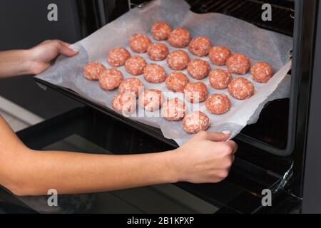 Weibliche Hände machen im Backofen Fleischbällchen. Schwedisches Rohmekatkugeln. Hausgemachte gebratene Rinderpatten. Auf Pergament gebacken Stockfoto