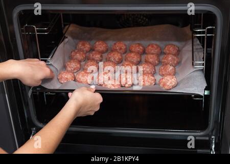 Weibliche Hände machen im Backofen Fleischbällchen. Schwedisches Rohmekatkugeln. Hausgemachte gebratene Rinderpatten. Auf Pergament gebacken Stockfoto