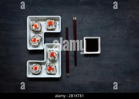 Japanisches krabbe mousse Sushi mit rotem Kaviar und Essstäbchen. Draufsicht, Nahaufnahme auf schwarzem Betonhintergrund Stockfoto