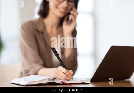 Kaukasische junge Frau, die telefonisch spricht und Notizen schreibt Stockfoto