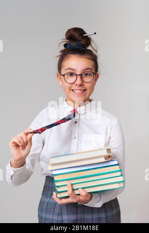 Ein wunderschönes und glückliches Mädchen liebt es zu studieren. Ein Schulmädchen mit Brille und Krawatte hält einen Stapel Bücher. Schulverein nach Klasse. Lernen Sie eine Fremdsprache. Stockfoto