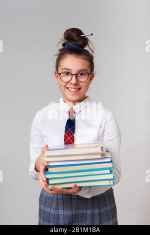 Ein hübsches und glückliches Mädchen im Teenager-Alter liebt es zu studieren. Ein Schulmädchen mit Brille und Krawatte hält einen Stapel Bücher. Richtige Ausbildung. Schulverein nach Klasse. Lernen Sie eine Fremdsprache. Stockfoto