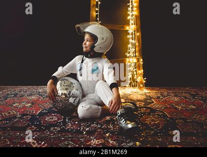 Astronautenfuturistisches Mädchen mit weißer Uniform in voller Länge und Helm mit silbernen Schuhen und Disco-Ball Stockfoto