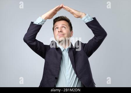 Fröhlicher zufriedener, gutaussehender junger Mann, der mit Dachgesten auf dem Kopf steht und mit tollem Lächeln aussieht. Studio aufgenommen, isoliert auf grauem Hintergrund. M Stockfoto