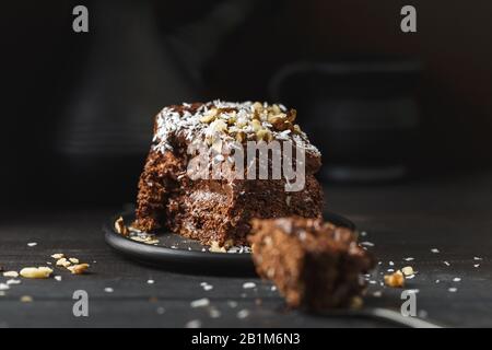 Ein Stück köstlicher Schokoladenkuchen in schwarzer Platte auf Holztischhintergrund, Nahaufnahme Stockfoto