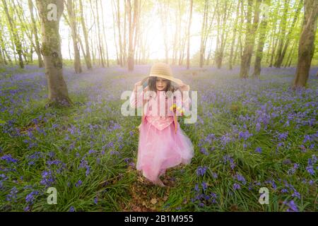 Ein junges Mädchen läuft durch Wald in Dorset mit bläugeln mit Sonne, die durch die buchen- und Birkenüberdachung von leuchtend grünen Blättern glänzen Stockfoto