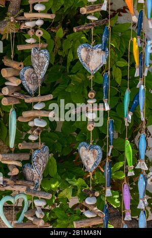 Dekorative hängende Mobiles aus Holz und Treibholz mit Herzen und Fisch, die in einem Geschenk- oder schäbigen schicken Homewares-Shop an einer Decke hängen. Stockfoto