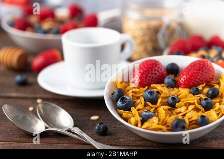 Gesundes Frühstück mit Cornflakes, Müsli und Cornflakes, mit Blaubeeren und Erdbeeren mit weißer Tasse hinten. Stockfoto