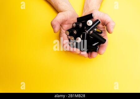 Viele schwarze aa-Batterien in männlichen Händen auf gelbem Hintergrund Stockfoto