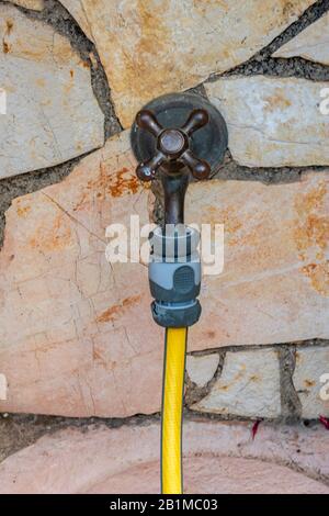 Ein alter Außenhahn aus Messing oder Wasserhahn mit einem gelben Schlauchrohr, der zum Bewässern des Gartens angebracht ist. Stockfoto