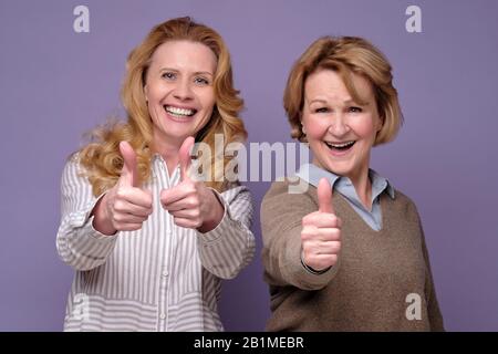 Zwei reife Frauen, die zwei Daumen hoch halten, um die Wahl zu genehmigen, die Ratschläge gibt. Studio gedreht Stockfoto