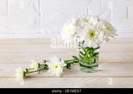 Kleiner bescheidener Blumenstrauß aus weißen, üppigen Chrysanthemen in einer Glasvase auf einem weißen Holztisch. Blumen- und Blumenschmuck. Kopierbereich. Stockfoto