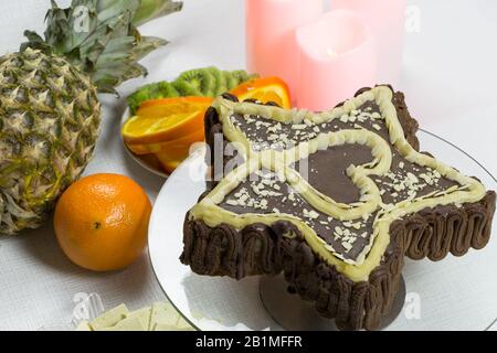 Dessert für einen geliebten Veganer für den Urlaub. Winkelansicht. Sternförmige Schokoladenkuchen mit Herz auf weißem Hintergrund. Kerzen, Ananas Stockfoto