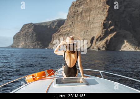 Frau, die mit Rettungswagen auf der Yacht sitzt und bei Sonnenuntergang in der Nähe der atemberaubenden Felsküste segelt Stockfoto
