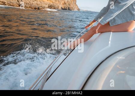 Frau, die auf einer Yacht in der Nähe der felsigen Küste segelt, schließt sich den Beinen an Stockfoto
