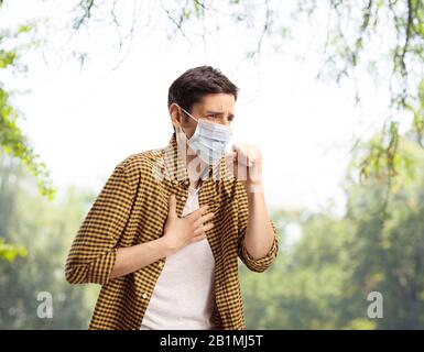 Junger Kerl hustet und trägt eine Gesichtsmaske im Freien in einem Park Stockfoto